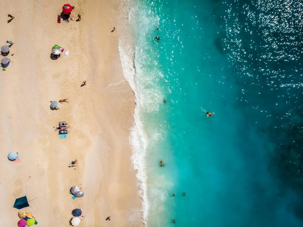 Drone aerial shot capturing sunbathers and turquoise waves on a sandy beach.